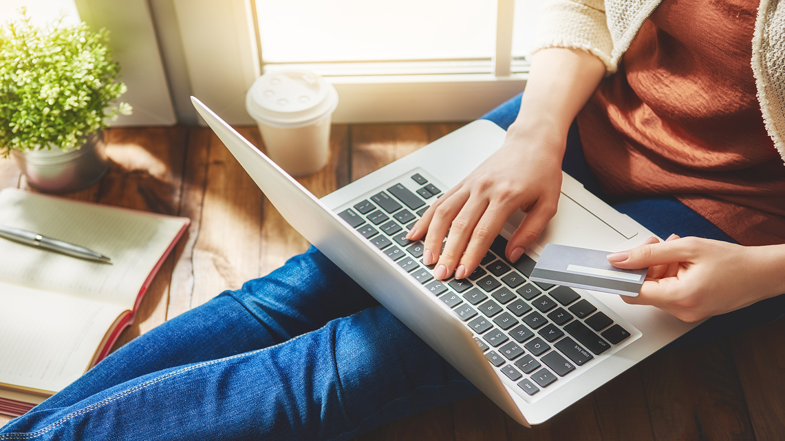 Person holding credit card while using laptop